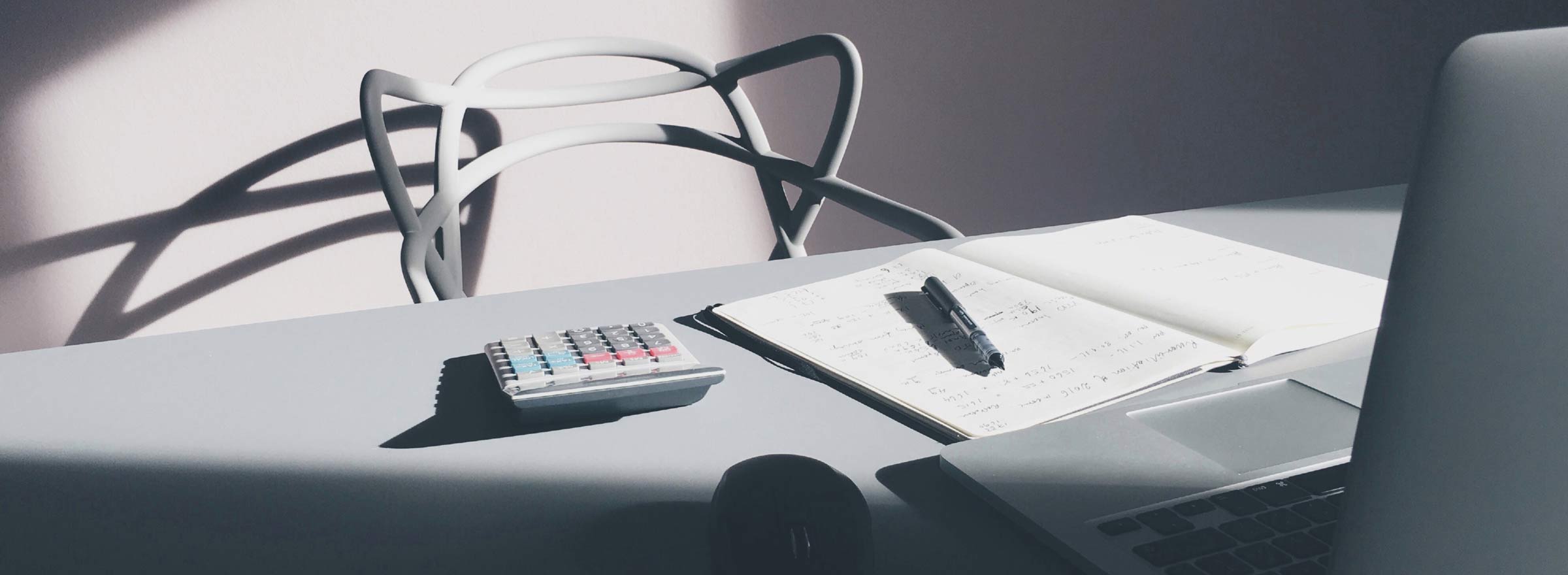 desk with an empty chair, a computer, a paper notebook, and a calculator