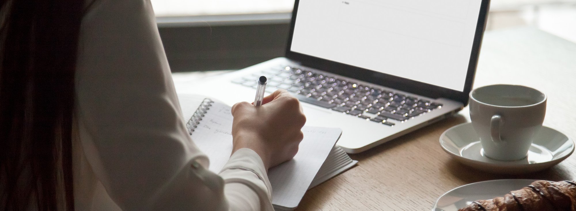 person using a pen to write notes in front of a computer